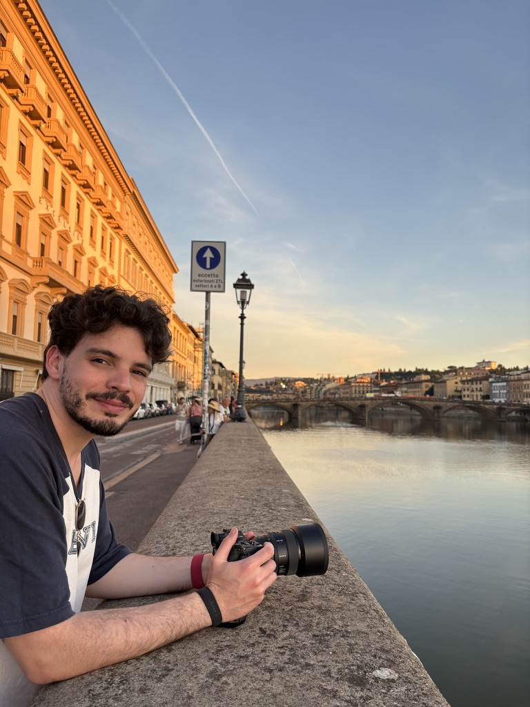 Rodrigo holding a camera beside a river at sunset.